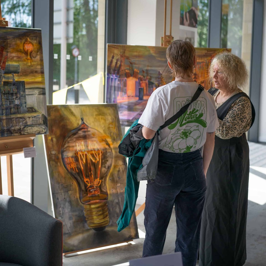 A photograph of two people standing in front of large paintings