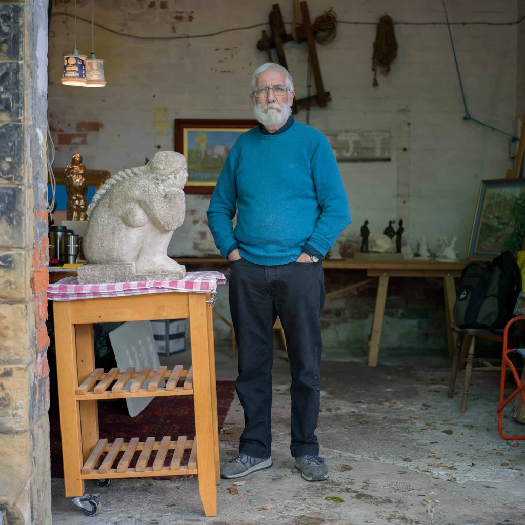 A photograph of a person standing in a workshop next to a small statue.