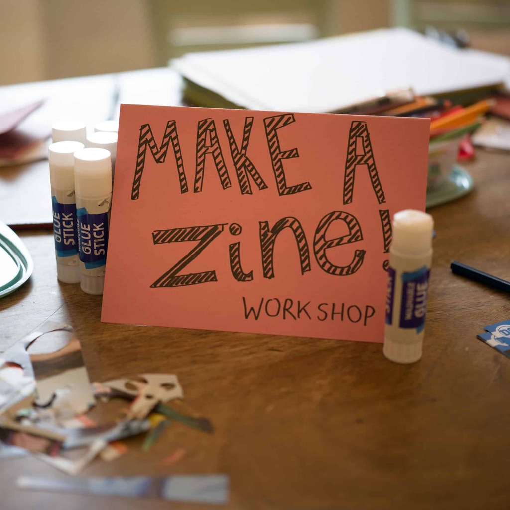 A photograph of a workspace with a sign reading, 'make a zine'.