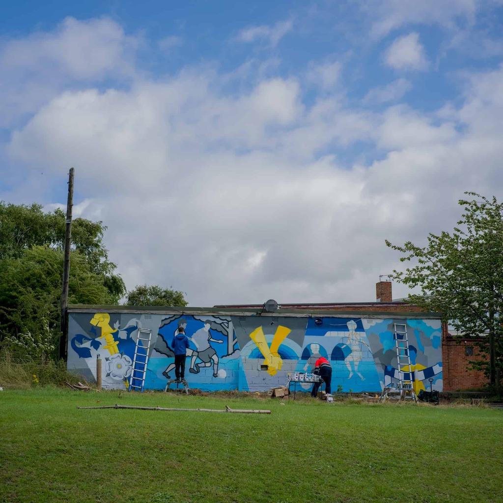 A photograph of a playing field wall painted with a mural