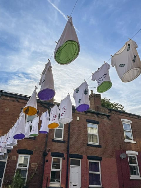 Looking up through the installation. A row of t-shirts, with art work emblazoned on them, are hanging high on a washing line between two back-to-back houses.