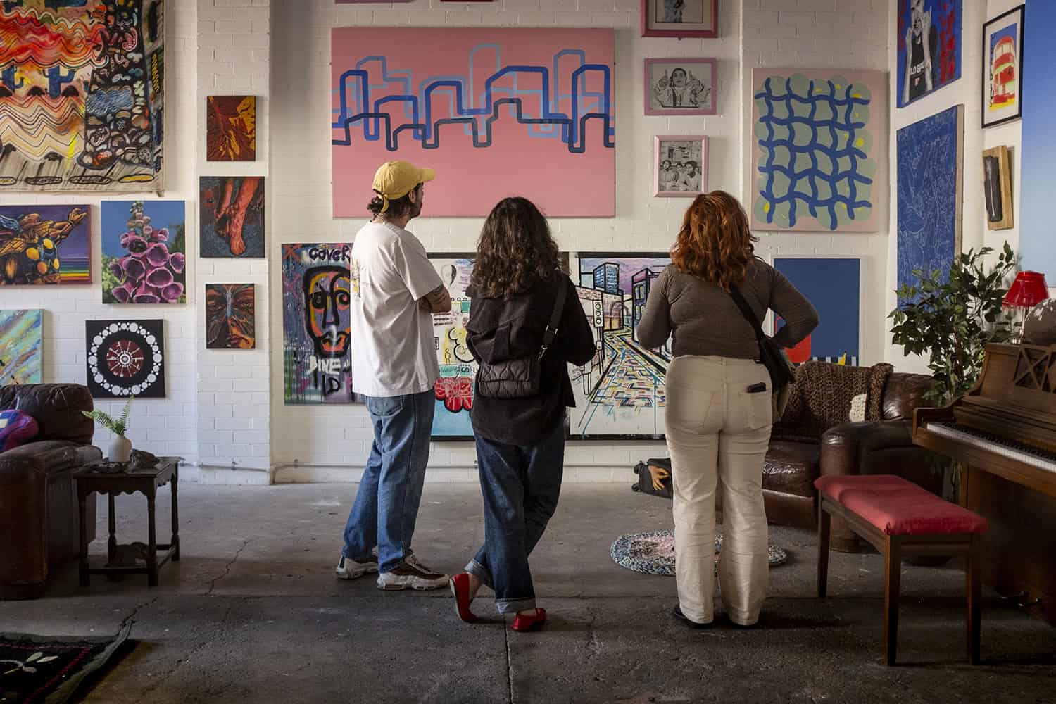 Three people stand looking at a gallery of art