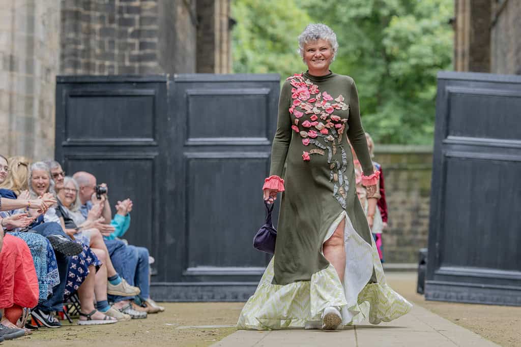 The model wears a long dress, it has been decorated with appliqués down the front.
