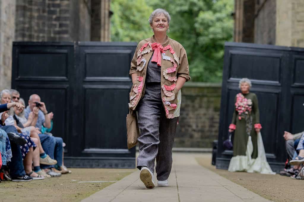 The model wears matching trousers and top. Over the top they wear a jacket which has been decorated with fabric appliqués
