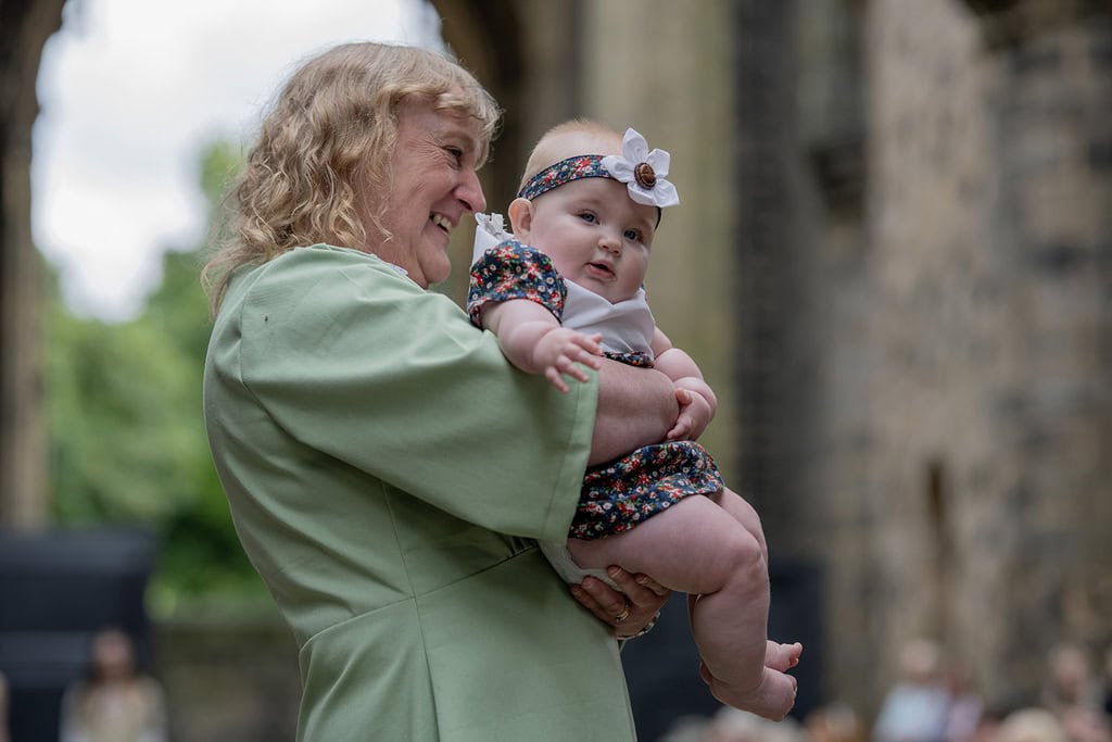 A baby, lifted up by a model, wears a dress and matching flower headband