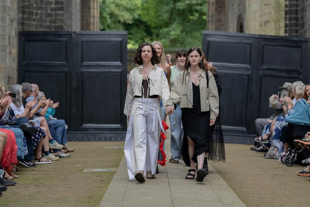 An audience watches designers and their models walk down the catwalk