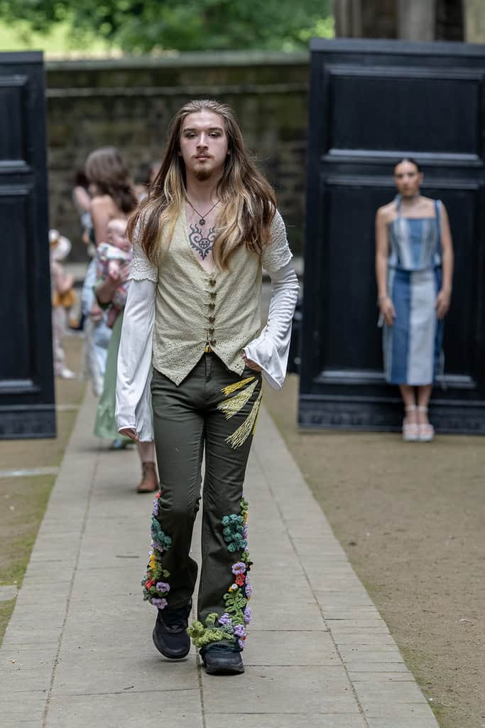 The model wears a loose sleeve shirt, and trousers decorated with appliqués