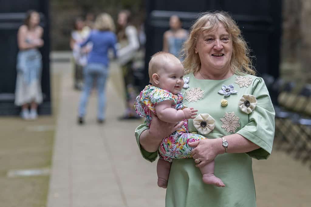 The model wears a dress that has been decorated with different appliqués. They are carrying a baby