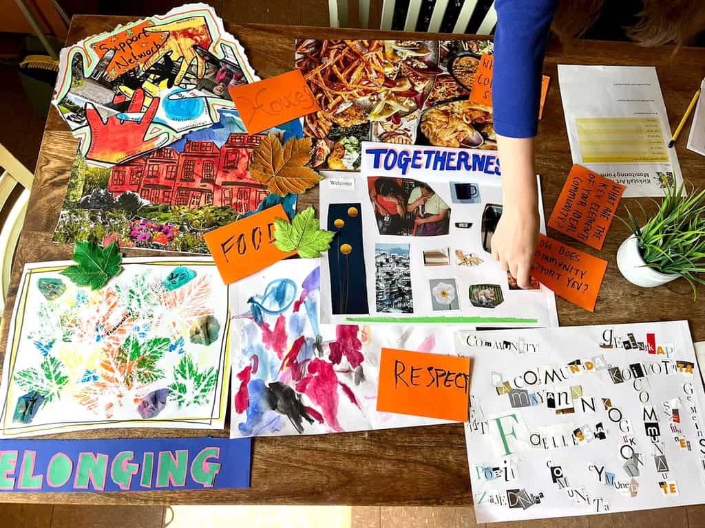 A table with a selection of work created during a community workshop. A person is placing words on the table.