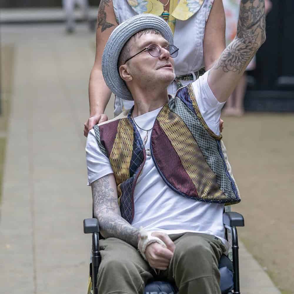 There are two models. The first in in a wheelchair waving to the audience, they wear a waistcoat made from ties. The other is pushing the chair and wears a dress