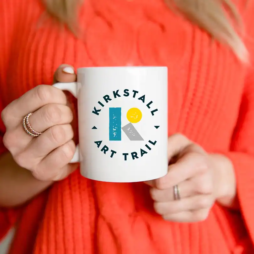 a person holds a white mug with the new Kirkstall Art Trail logo
