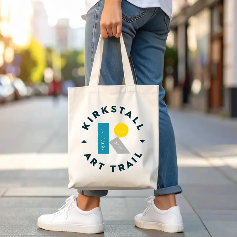 a person holds a canvas tote bag printed with the new Kirkstall Art Trail logo